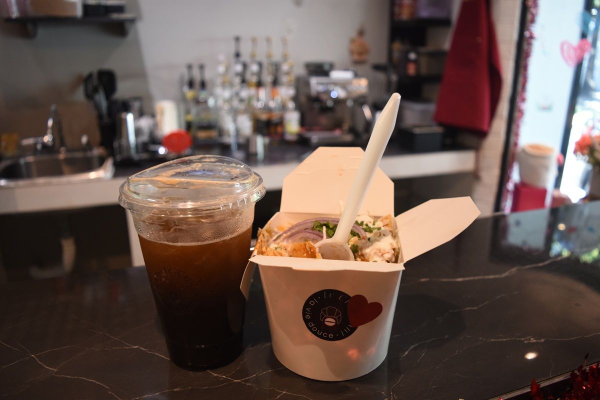 Chilaquiles en su caja blanca con la estampa de Le Croissant, junto a un café en las rocas, sobre la barra de mármol negro.