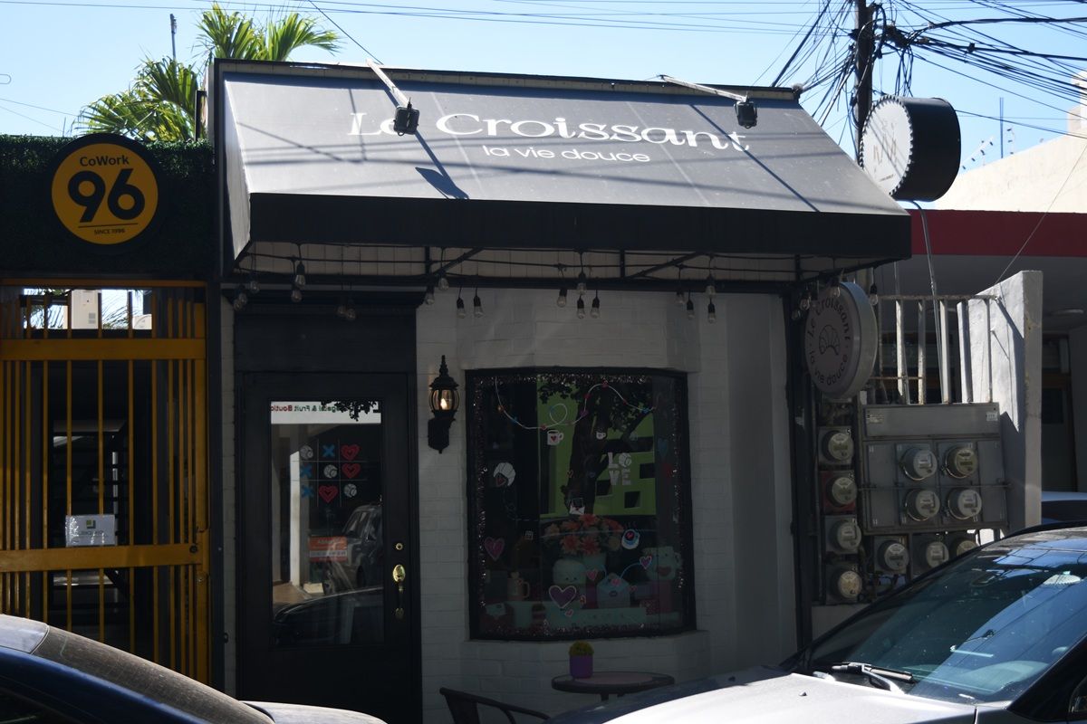 La fachada de Le Croissant: toldo negro con el nombre y 'la vie douce', pared de ladrillo blanco, puerta negra y el letrero redondo.